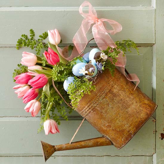 Um regador cheio de flores vira guirlanda de porta com a ajuda de uma fita de decoração