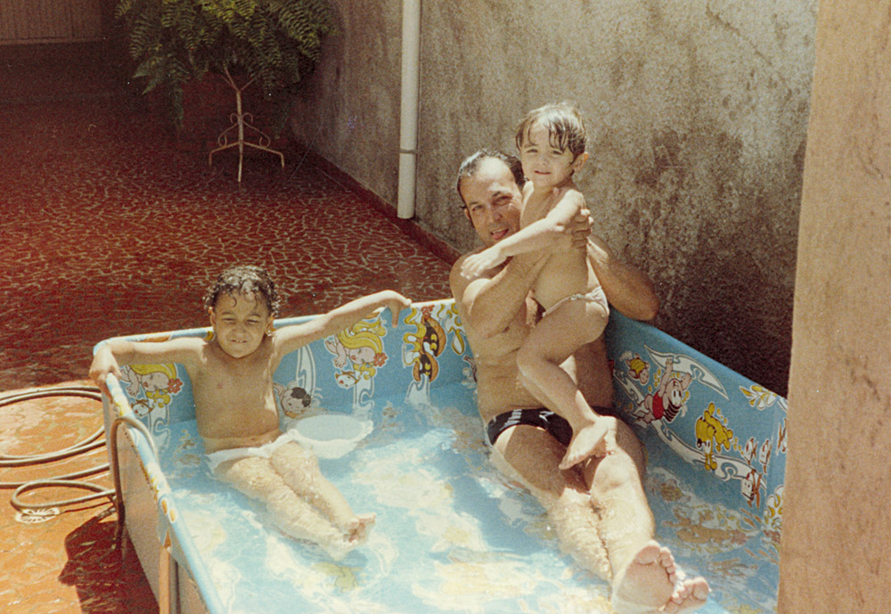 Aos 4 anos, no colo do pai, Joaquim, com a irmã, Aline, se refrescando na piscina da Turma da Mônica, no quintal da casa onde cresceu