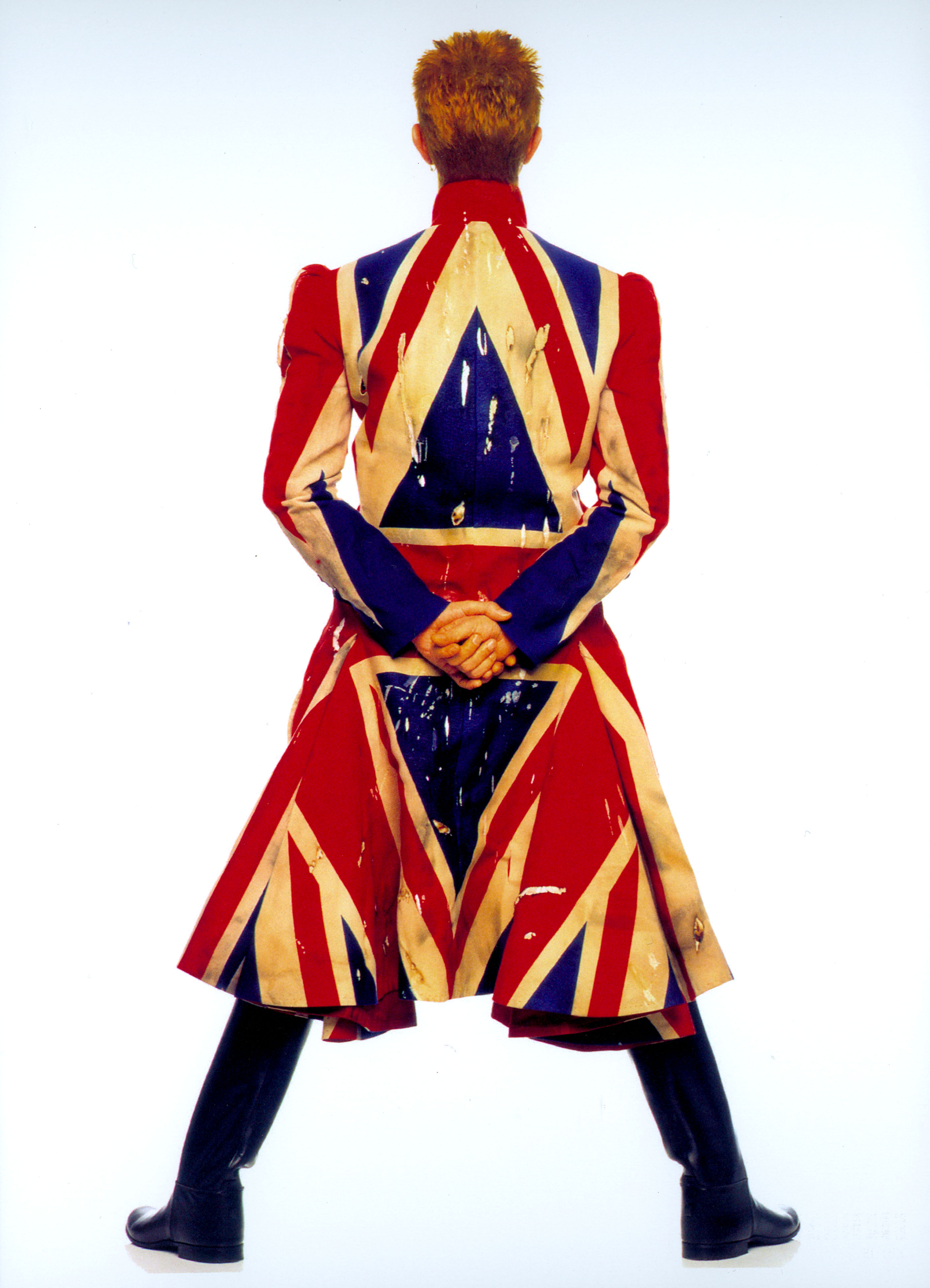 TRENCH COAT COM A BANDEIRA DA INGLATERRA USADO NA TURNÊ DO ÁLBUM “EARTHLING” (1997) Provando o bom exemplo de Homem Inglês que é, em momento ufanista chic vestindo um casaco assinado pelo estilista Alexander McQueen! Assim como Bowie, a Inglaterra personifica naturalmente extravagância & exuberância.