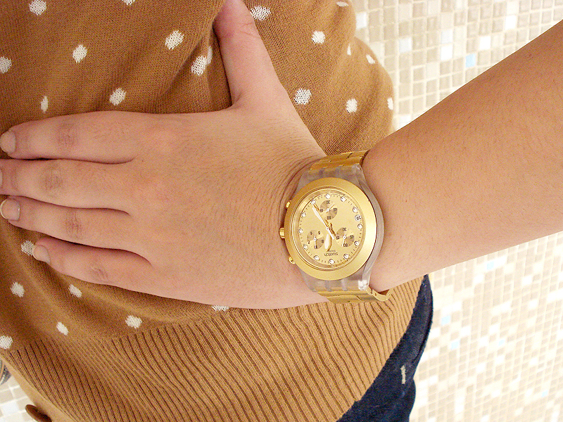 Detalhe no relógio dourado da Swatch que se encaixa bem com as cores frias do look.