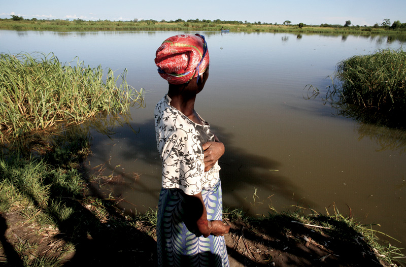 Pela primeira vez em nove anos, a mulher da foto, também moradora das redondezas do rio Shire, no Malauí, retorna ao lugar onde foi atacada por um crocodilo quando enchia baldes de água. Este rio tem 402 quilômetros de extensão e suas águas são funda