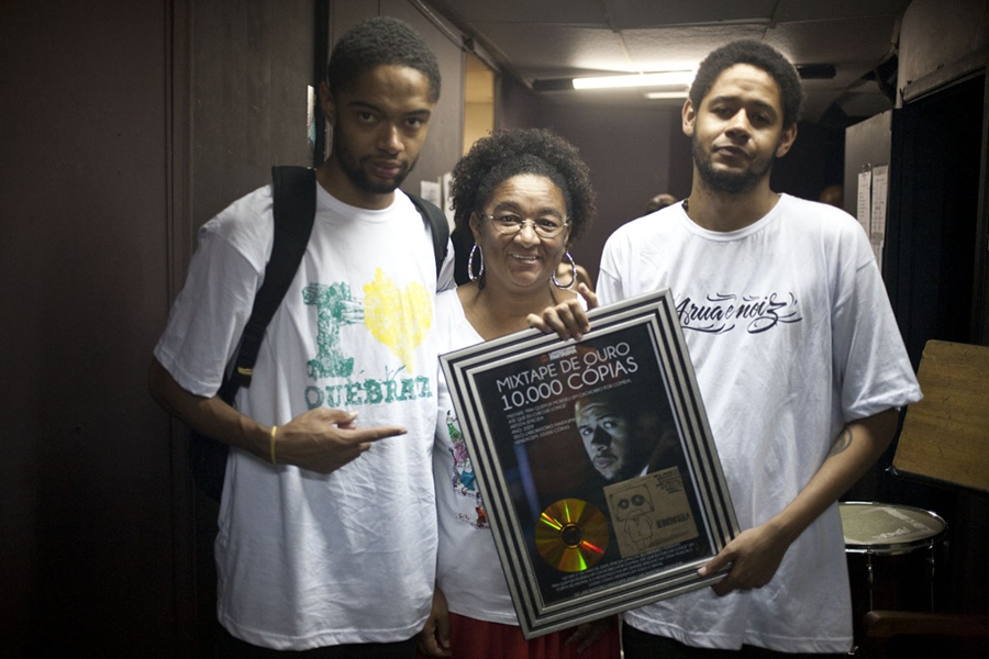 Evandro, Jacira e Leandro seguram a placa que eles mesmos fizeram e se autoconcederam comemorando a “mixtape de ouro” por 10 mil cópias vendidas