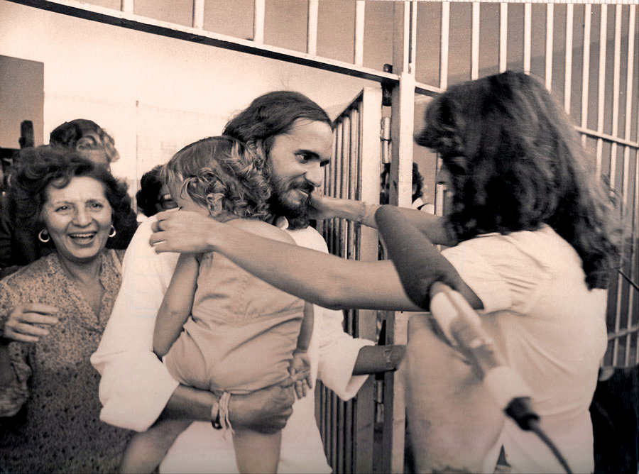 Com o filho nos braços, reencontrando a esposa e a mãe (sorrindo atrás dele) após ser libertado