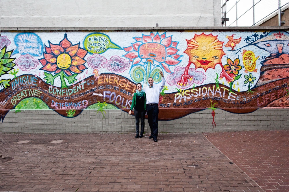 Paula e o professor Ritz na frente do mural pintado por alunos