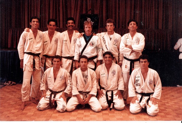 foto de Rorion Gracie com o aluno Chuck Norris (de pé), Rickson Gracie (ajoelhado) e alguns praticantes célebres do jiu-jítsu em seus primórdios