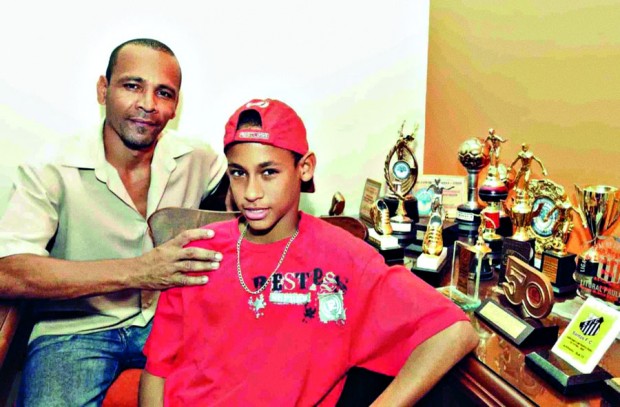 Neymar pai e Neymar filho no antigo apartamento ao lado da Vila Belmiro, com os troféus do atacante