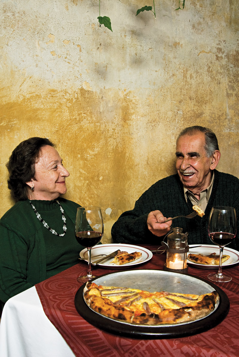 Silvio Frangella comendo uma pizza de aliche e tomando um vinho com a esposa