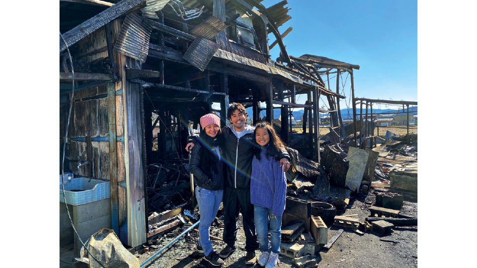 Rodrigo, a esposa, Andréia, e a filha, Naomi, sorriem em frente à sua casa, destruída por um incêndio. "Ninguém pediu, foi natural para cada um de nós sorrir"