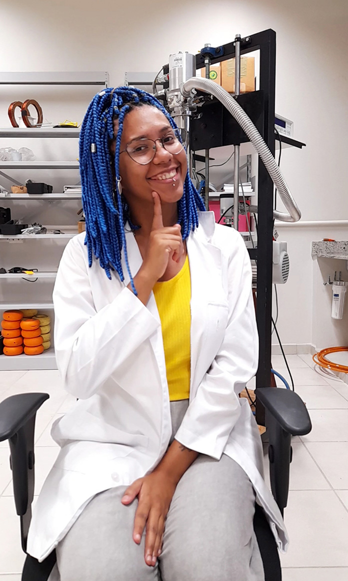 No laboratório, a física Carleane Patrícia posa de avental branco e cabelo azul