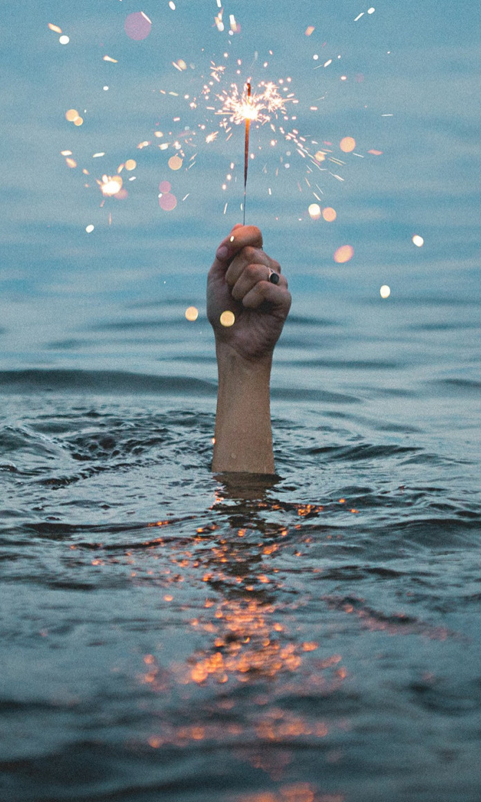 No meio do mar, uma mão está para fora da água segurando uma vela acesa