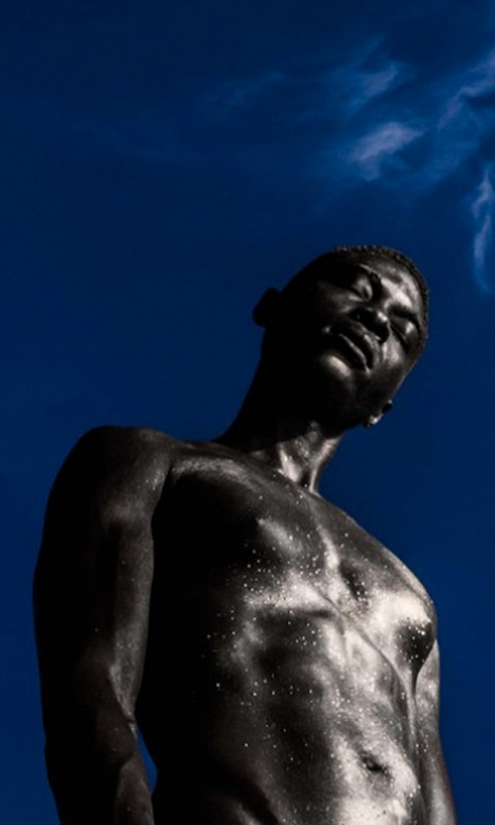 À frente de um céu azul, homem negro está em pé de olhos fechados, foto que faz parte do projeto Black Is Beautiful