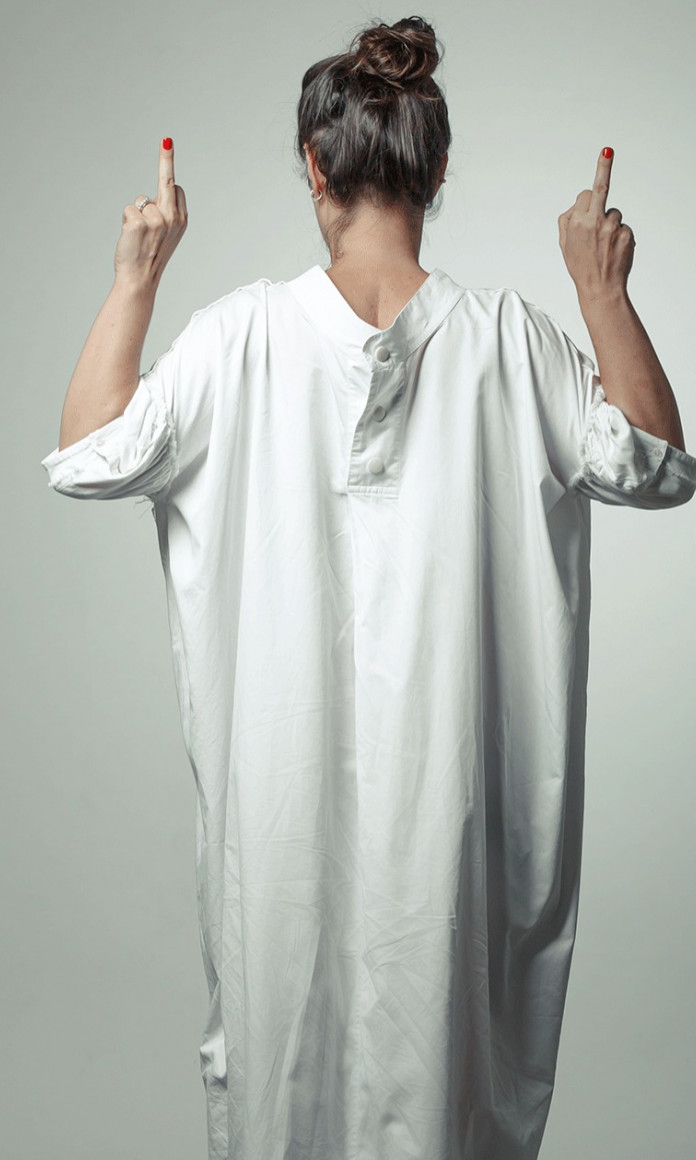 mulher grisalha com vestido branco, de costas, mostra o dedo do meio