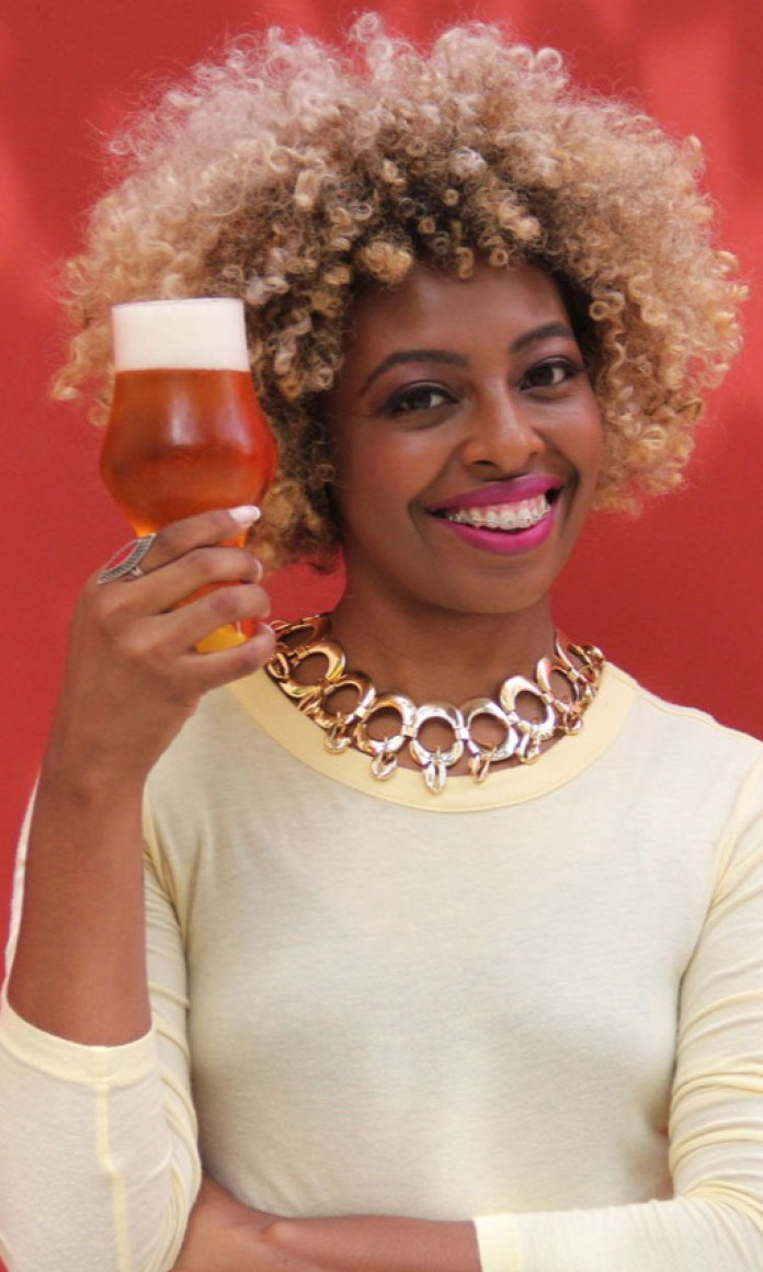 Mulher com cabelo black power loiro segura um copo de cerveja na frente do rosto