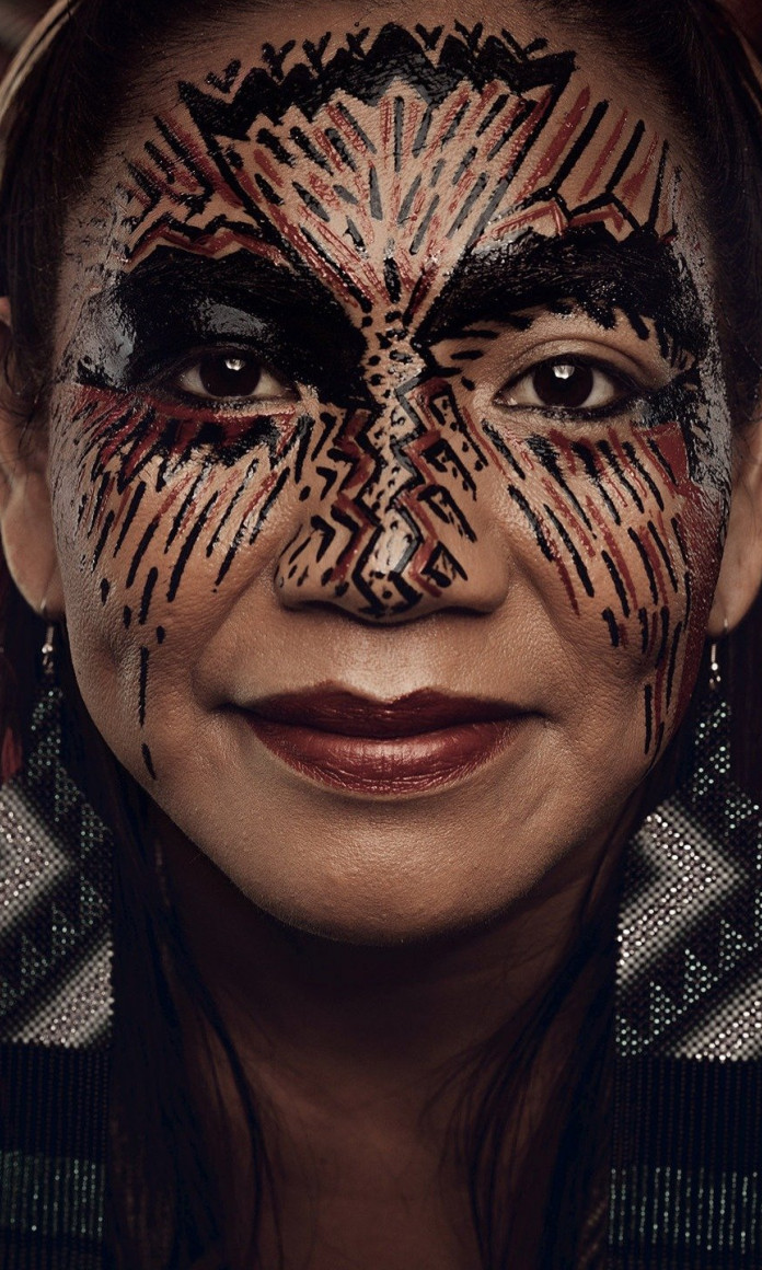 Mulher indígena tem a cara pintadas com traços vermelhos e pretos