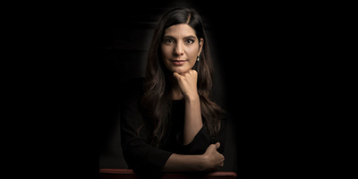 Andréia Sadi fotografada em um fundo preto, sentada e com as mãos apoiadas no rosto