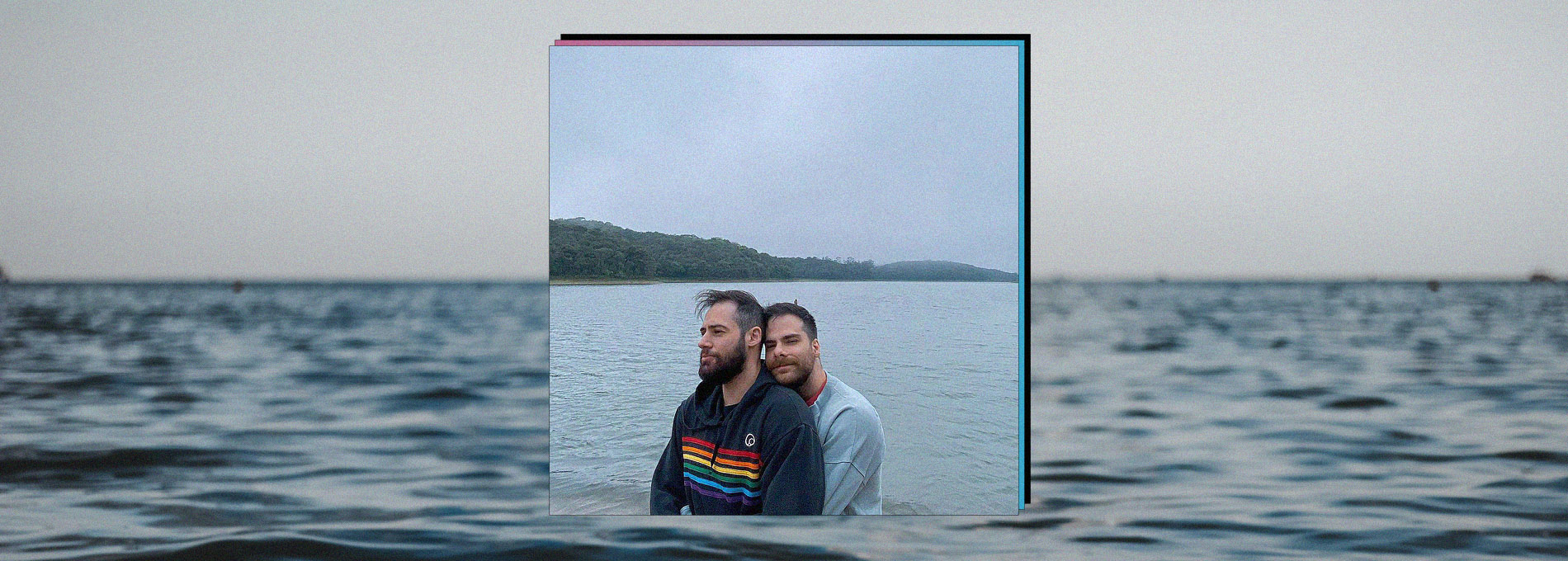 Paulo Vaz sendo abraçado por Pedro HMC em frente a um lago, céu cinza e dia frio