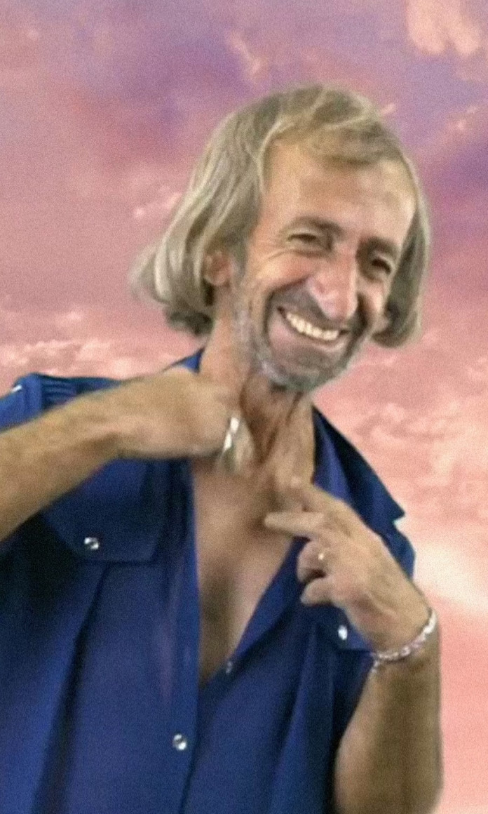 Senhor de cabelos compridos e barba usa camisa azul em frente a um fundo de céu roxo
