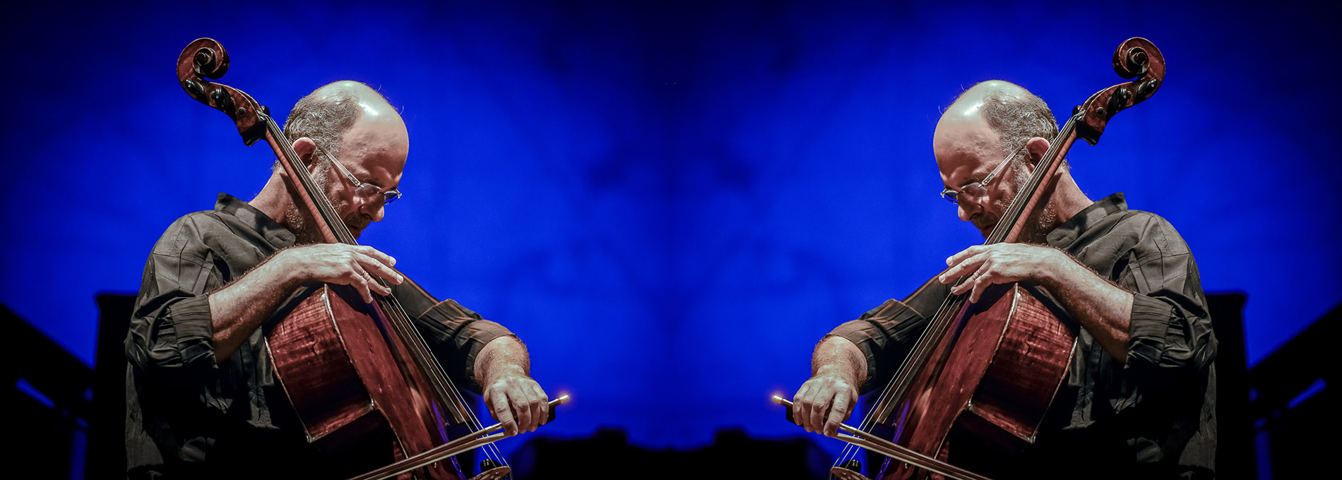 Jaques Morelenbaum tocando violão cello em um palco iluminado e com um fundo azul