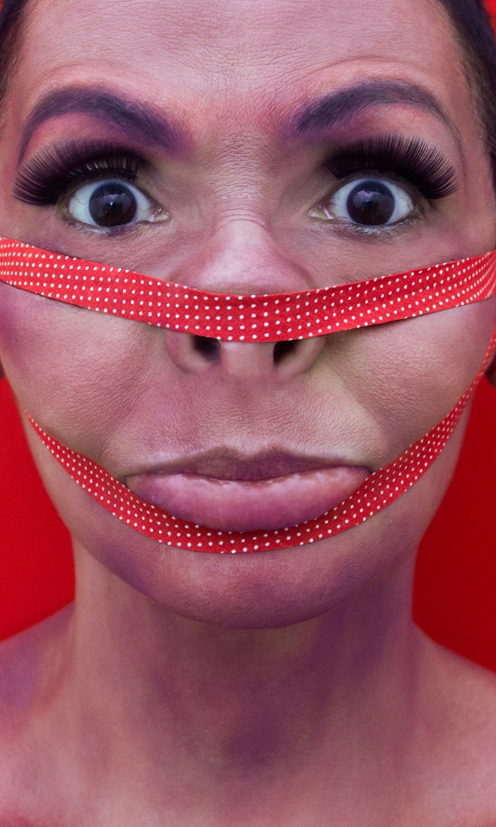 Rosto de uma mulher branca com fitas vermelhas apertando seu nariz e seu queixo