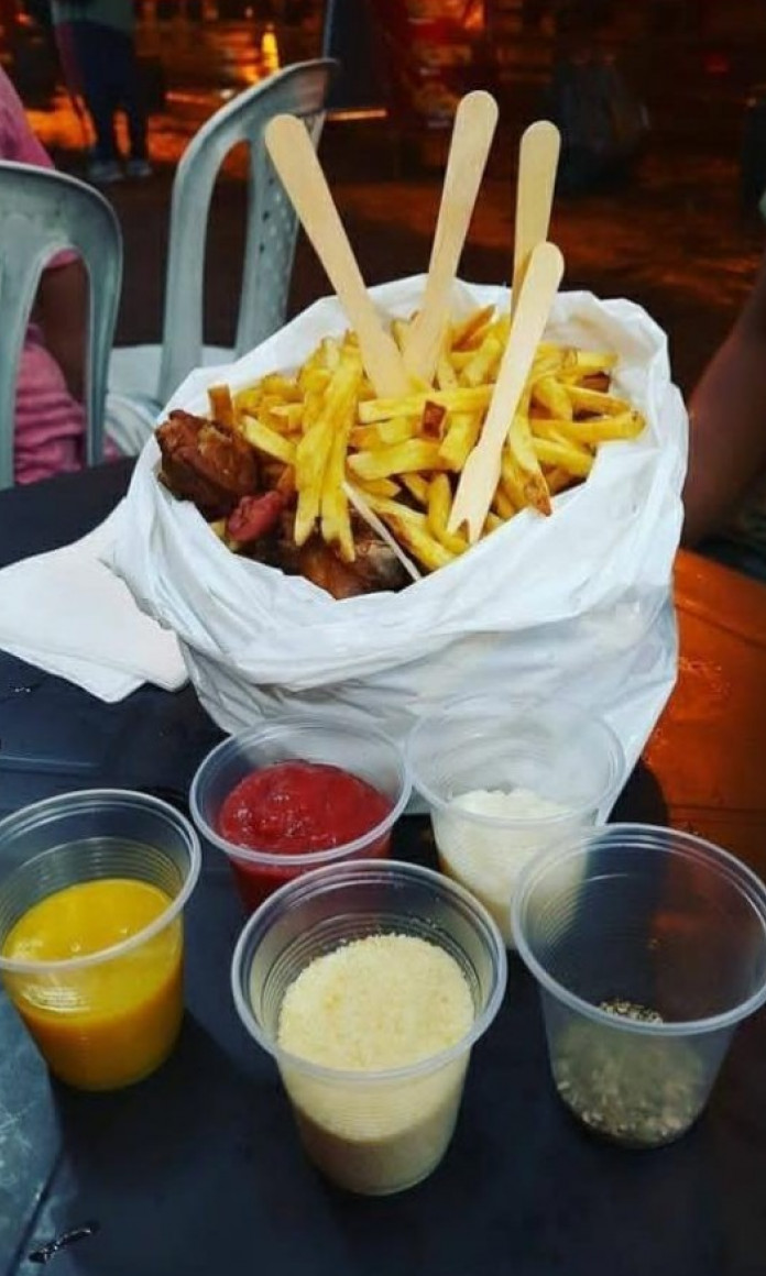 Saco plástico cheio de batatas fritas e bacon em cima de uma mesa cercada com molhos