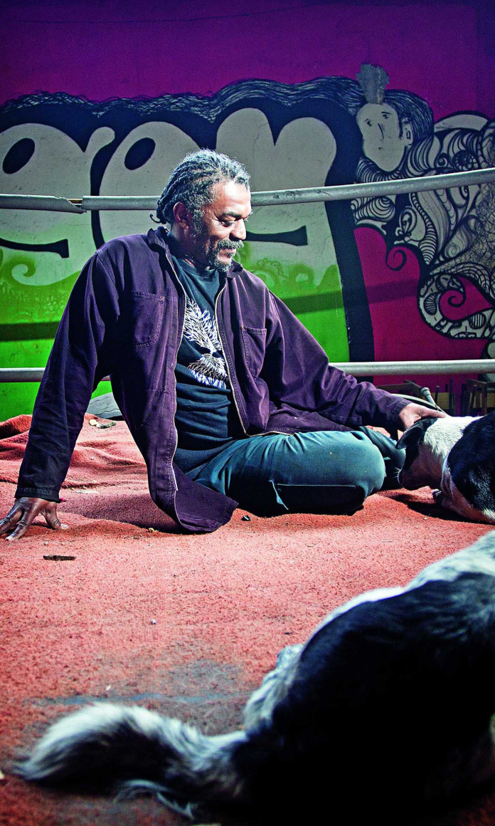 Homem sentado em um ringue de boxe cercado por cachorros
