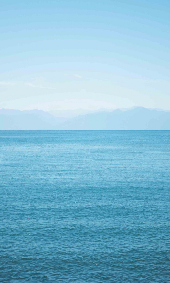 Mar azul com sombras azuis de montanhas no horizonte