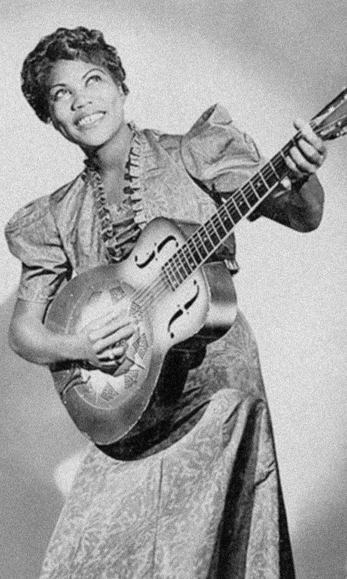 Mulher negra com vestido e cabelos presos segurando uma guitarra numa foto antiga