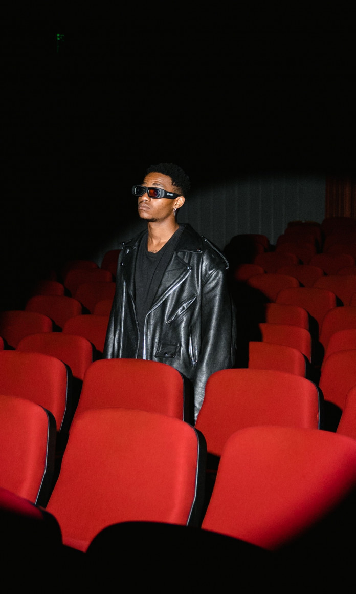 Homem negro sozinho no meio de um cinema, cercado de cadeiras vermelhas