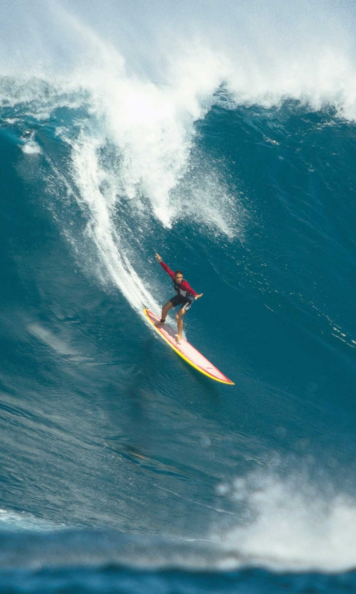 Mulher surfista numa prancha pegando uma onda gigante no Havai
