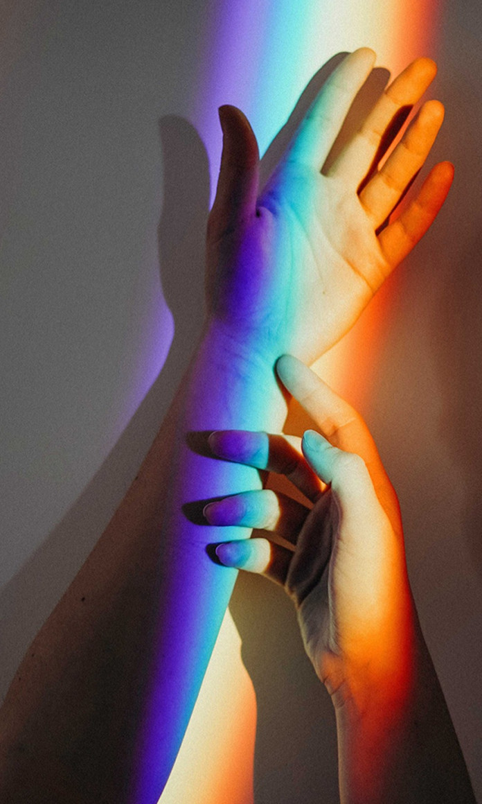 Mão e braço iluminado por um faixo de luz arco iris