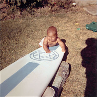 O bebê Adam com dois símbolos dos Paskowitz, a prancha e a estrela de Davi