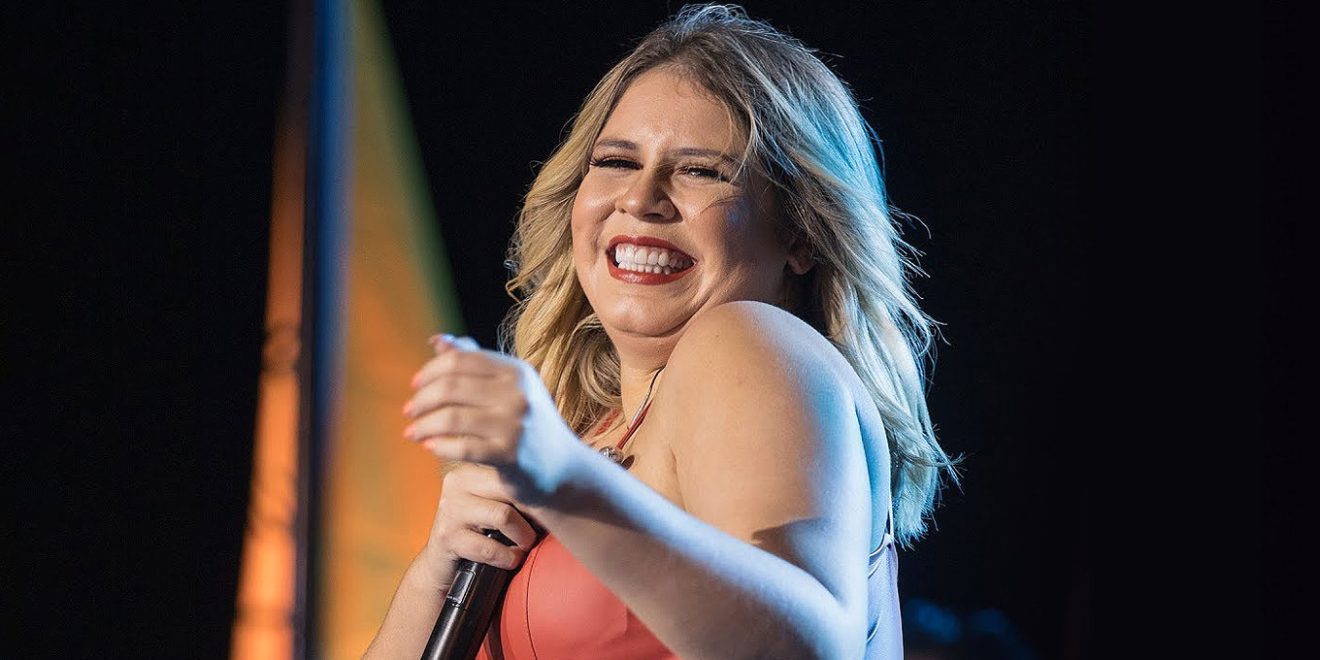 Marília Mendonça no palco cantando e sorrindo