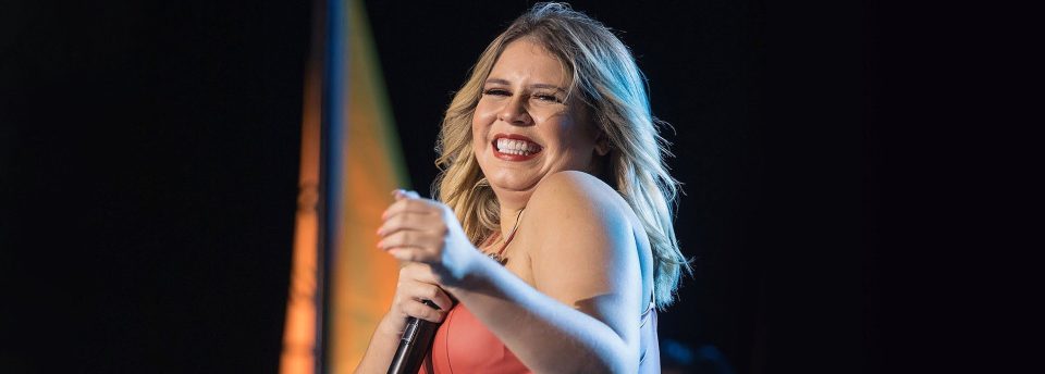 Marília Mendonça no palco cantando e sorrindo